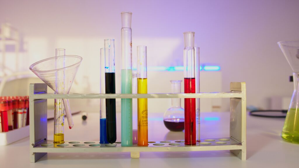 Colourful chemistry lab glassware with test tubes of coloured liquid, representing sunscreen and UV-filter formulation testing at a South Korean cosmetics ODM factory.