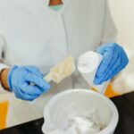 Laboratory technician in gloves mixing a white skincare cream in a bowl, illustrating cosmetic manufacturing in Malaysia